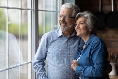 Happy bonding loving middle aged senior retired couple standing near window.